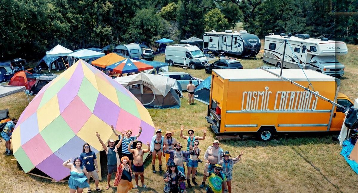 Aerial view of the Cosmic Creatures installation: participants waving beside the pastel Cosmic Zome and the orange Cosmic Creatures truck