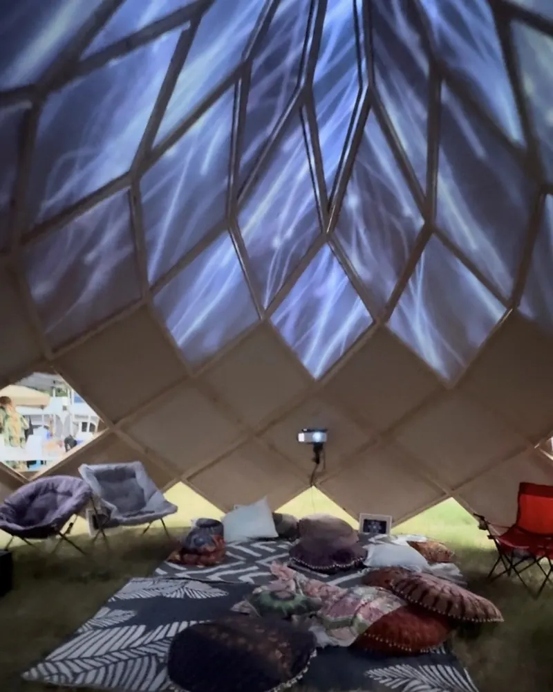 Inside the Cosmic Zome: blue light projections across the dome's geometric panels above floor cushions, rugs and chairs